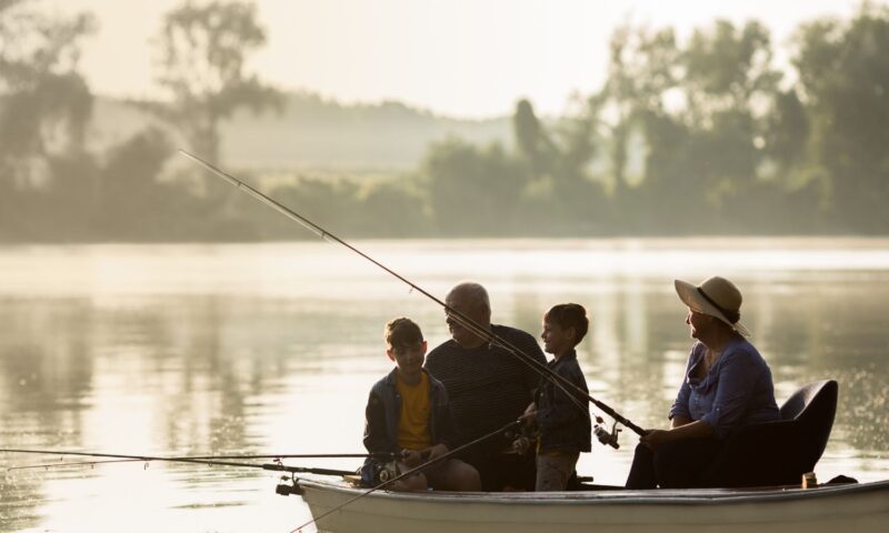 Family of four fishing from a boat on a calm lake in Louisiana at sunrise.
