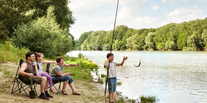 Boy holding a fishing rod with a fish, as family watches from chairs on a bayou riverbank in Louisiana.
