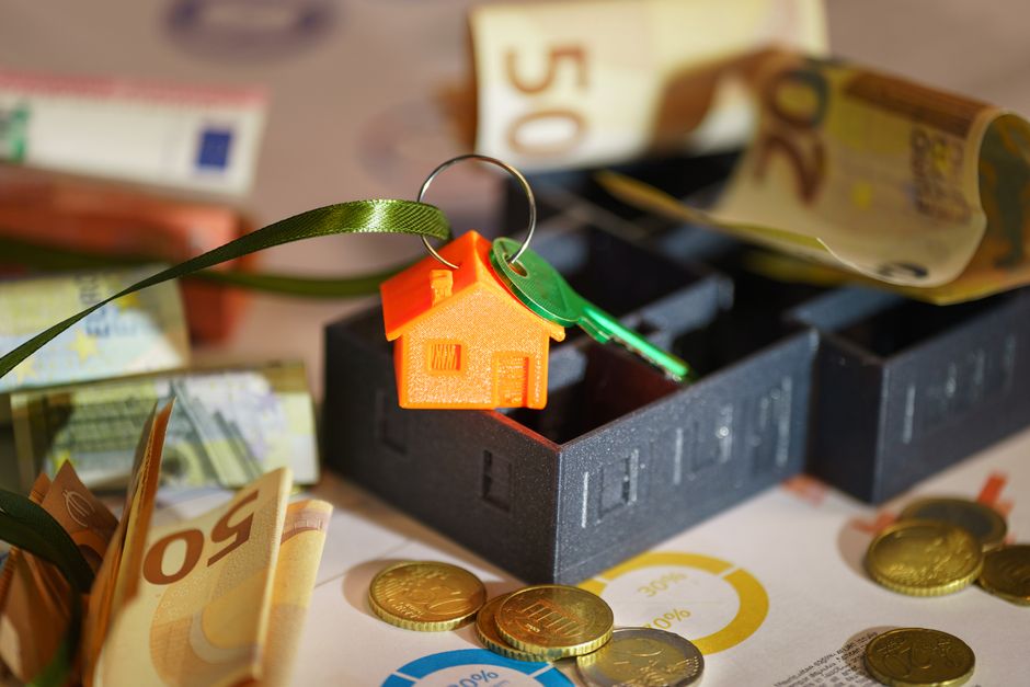 A minimalist photo of a small wooden house model sitting next to stacks of coins on a clean background, symbolizing the various costs associated with selling a property.