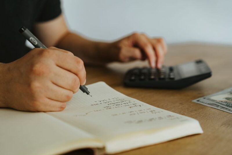 Person's hands using a calculator over house blueprints and financial documents on a bright, modern desk, representing the...